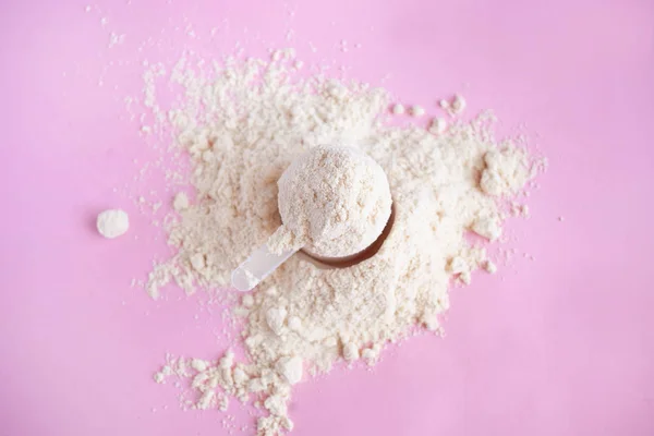 Mucchio di proteine del siero di latte in polvere con cucchiaio di plastica su sfondo rosa vista dall'alto — Foto Stock