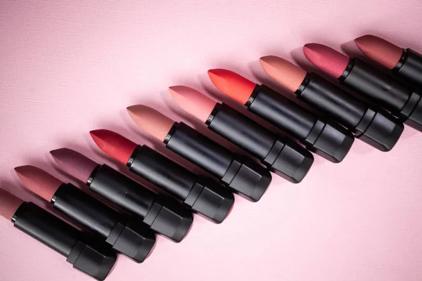 Many lipstick in different natural colors on a pink background. Top view with selective focus — Stock Photo, Image