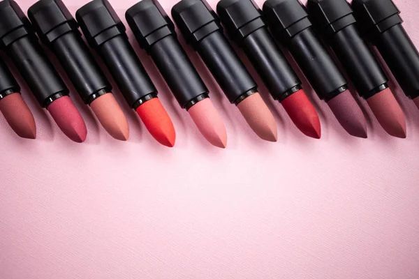 Lipstick in different natural colors in a row at the top of the picture on a pink background. Top view with selective focus — Stock Photo, Image