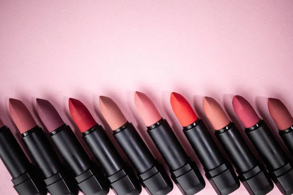 Lipstick in different natural colors in a row at the bottom of the picture on a pink background. Top view with selective focus — Stock Photo, Image