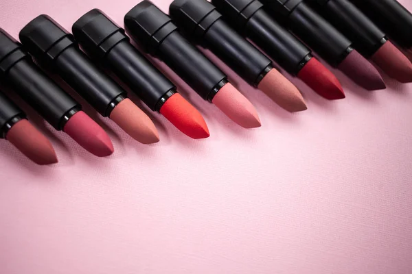 Lipstick in different natural colors in a row at the bottom of the picture in a row diagonally on the top of the picture on a pink background. Top view with selective focus copy space — Stock Photo, Image