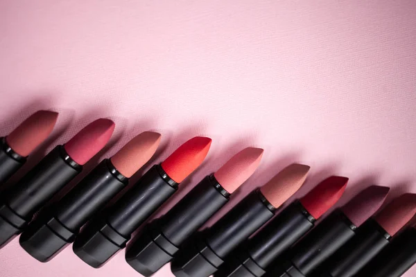 Lipstick in different natural colors in a row at the bottom of the picture in a row diagonally at the bottom of the picture on a pink background. Top view with selective focus copy space — Stock Photo, Image