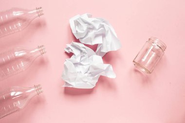 Belediyenin katı atıkları. Üç plastik şişe, buruşmuş kağıt ve pembe arka plan manzaralı bir cam kavanoz.