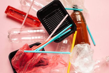 Çevre sorunları ve çevresel koruma. Pembe arka planda plastik tek kullanımlık paketleme ve plastik kokteyl pipetleri yığını