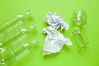 Belediyenin katı atıkları. Üç plastik şişe, buruşmuş kağıt ve yeşil arka planda iki cam kavanoz.