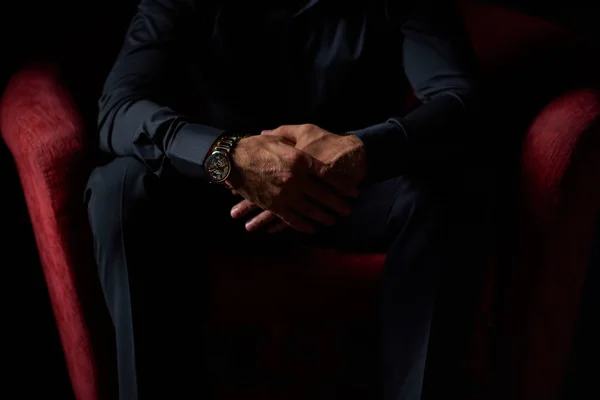 male businessman in a black suit sitting in red chair, black background, no faces visible, studio shooting