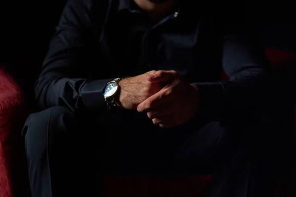 male businessman in a black suit sitting in red chair, black background, no faces visible, studio shooting