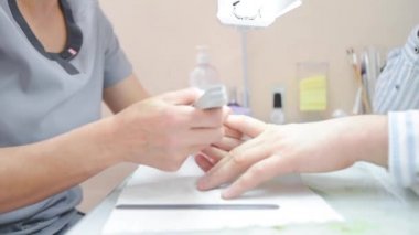 Bir manikürcü bir adamın tırnaklarını keser.