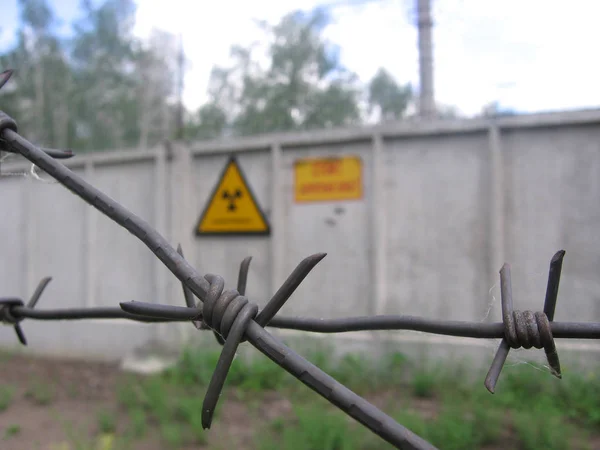 Sign of radiation on the grey fence of the restricted area with barbed wire