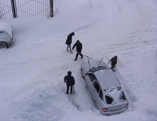 何人かの人々が雪の駐車場で立ち往生した車を掘り起こす — ストック写真