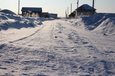 Kışın Sibirya 'da bir köyde kirli karla kaplı evlere giden yol.