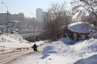 Rusya, Novosibirsk, 21 Şubat 2015. Bir kadın, kışın meyilli bir yolda yürüyor. Bir ara sokaktaki ahşap evlerin yanından geçiyor.