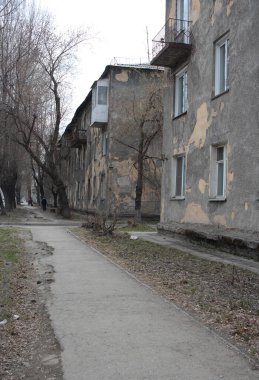 Tozlu, kirli bir şehirde, sonbaharda çok katlı gri bir evin yanında boş, dağınık bir yol.