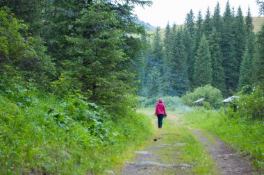 Genç bir kadın dağlarda bir patikaya gider. Güzel bir manzara.