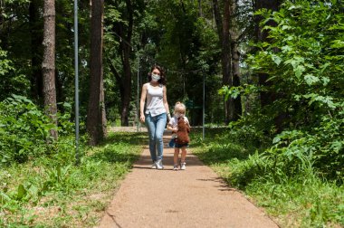 Anne ve kızı, salgın günlerinde parkta maskeyle dolaşıyorlar. Karantina