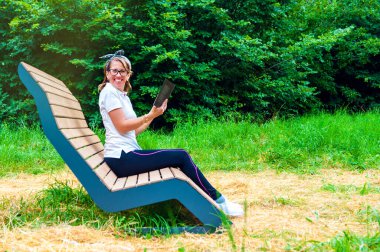 Ormanda kitap okuyan genç bir kadın. Mutlu kadın gülümsüyor