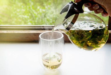 Çaydanlıktan şeffaf bardağa dökülen yeşil çaya yakın çekim