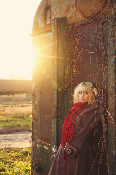 Young girl in leather coat with camera near railroad in sunshine, sunrise