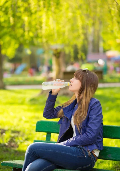 公園のベンチに座って待っているハンドバッグと美しいファッション女性と水を飲む — ストック写真