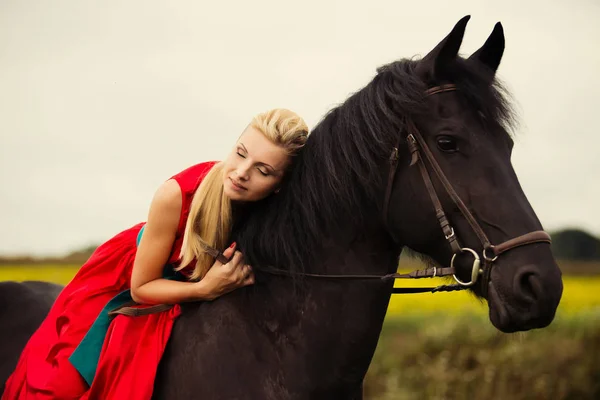 Mujer rubia de moda montando un caballo en un día soleado. Cabello largo . — Foto de Stock