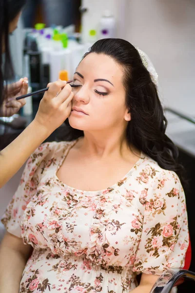 Junge schöne Braut beim Hochzeits-Make-up von Visagistin Stockbild