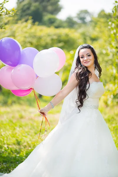 Счастливая ошеломляющая невеста в платье с красочными шариками в зеленом парке — стоковое фото