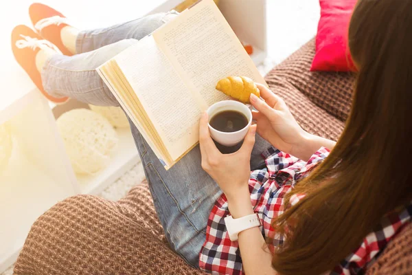 Ona kahve kupa oturma odasında evde tutan bir kitap okuma kanepede oturan kadın