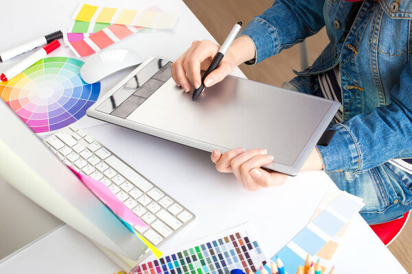 young woman artist in jeans jacket drawing something on graphic tablet at the office