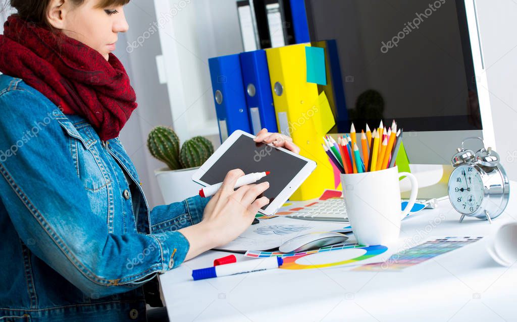 young woman artist in jeans jacket drawing something on graphic tablet at the office