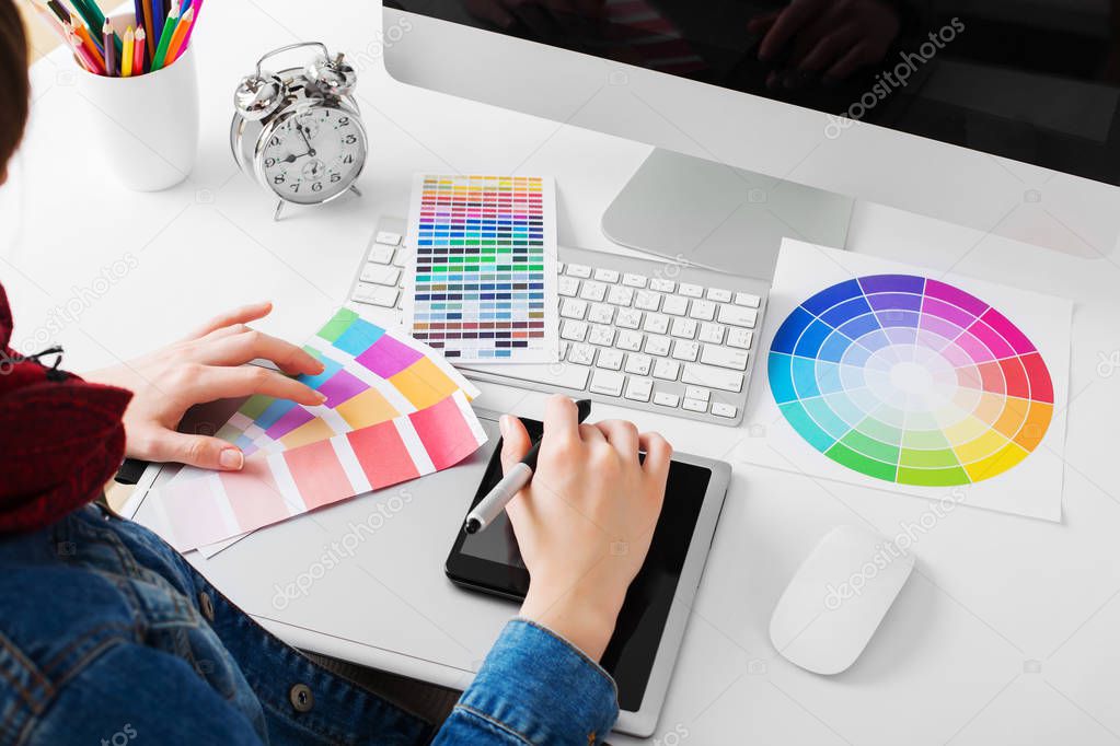 young woman artist in jeans jacket drawing something on graphic tablet at the office