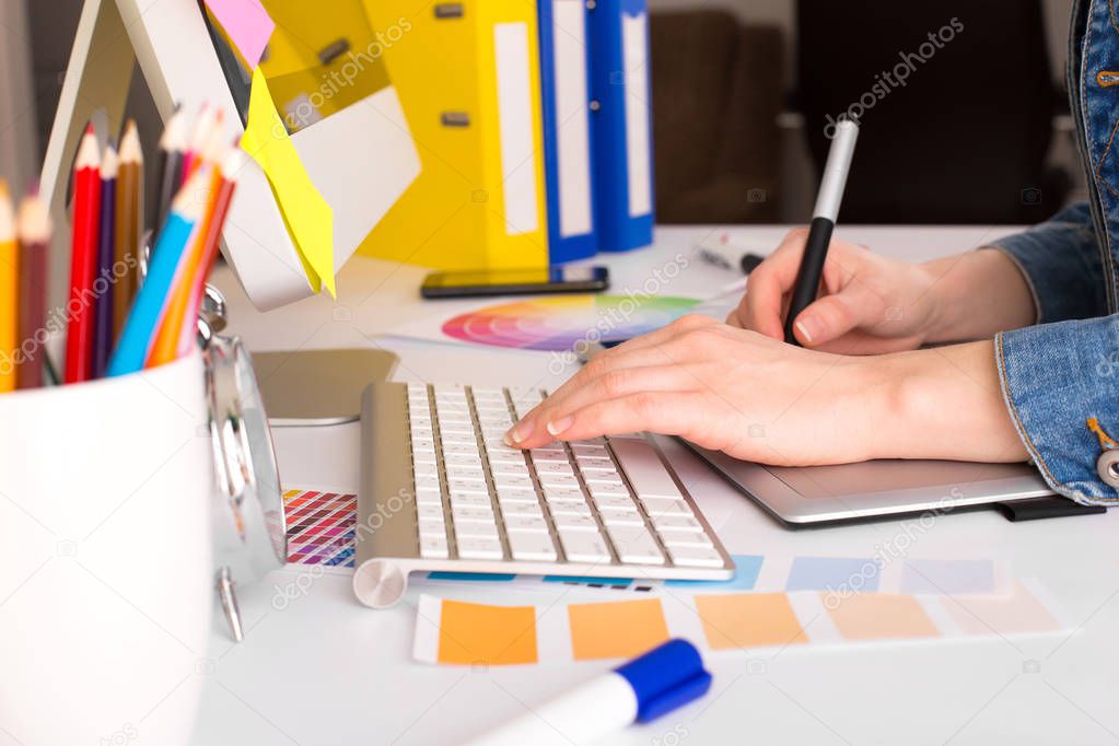 young woman artist in jeans jacket drawing something on graphic tablet at the office