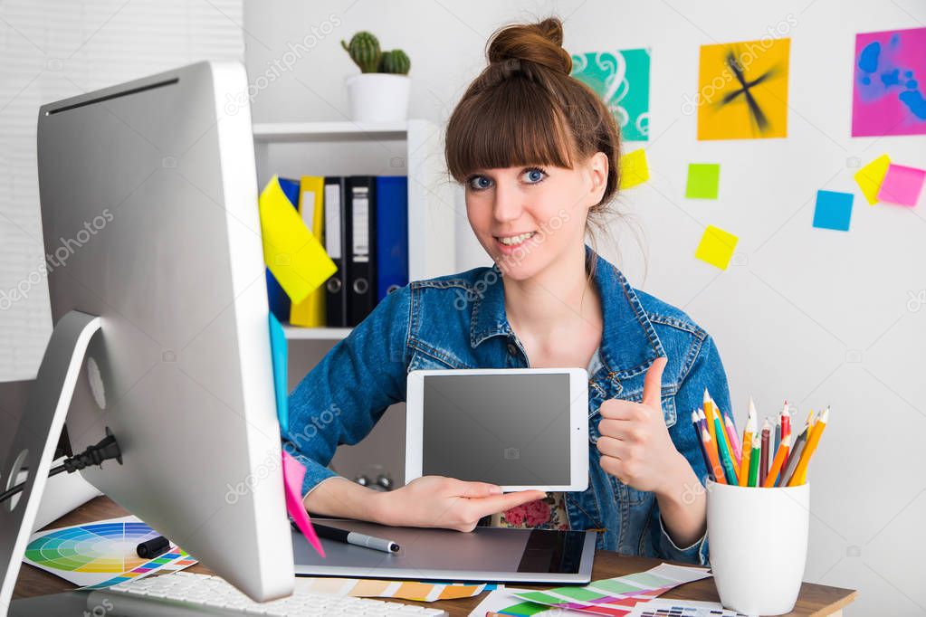 young woman artist in jeans jacket drawing something on graphic tablet at the office