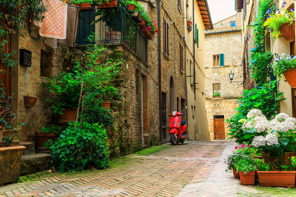Spectacular traditional decorated street with flowers and rustic houses, old fashioned scooter standing in typical Italian street, Pienza, Tuscany, Europe