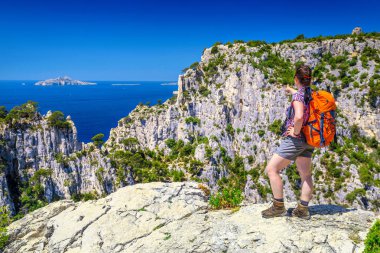Sırt çantası ve fotoğraf kamera yüksek kayalıklarla görünümünden zevk mutlu uzun yürüyüşe çıkan kimse kadınla. Kadın bakış açısı Cassis, Calanques Milli Parkı, Provence, Fransa, Avrupa yakınındaki üstünde duruyor