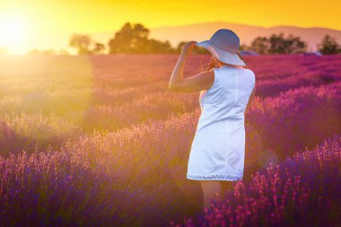 Beyaz elbise ve doğanın, lavanta alanları batımında keyfini hasır şapka neşeli genç kadın. Yaz manzara renkli mor lavanta alanları ve mutlu kadın kavramı, Valensole, Provence bölgesi, Fransa, Avrupa ile 