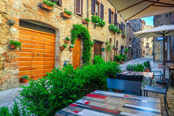 Narrow Tuscany street with stone houses and flowery entrances. Cozy street cafe with colorful tables and traditional stone houses, Pienza, Tuscany, Italy, Europe