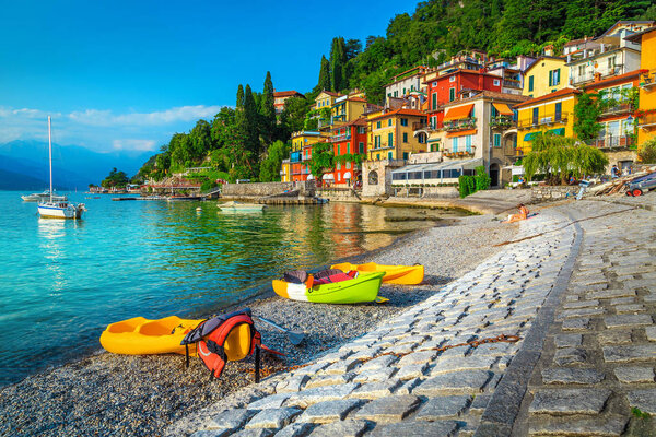 Famous travel and tourism location with colorful buildings. Summer holiday resort with colorful canoes, kayaks and boats, Varenna, lake Como, Italy, Europe. Vacation and relaxation concept