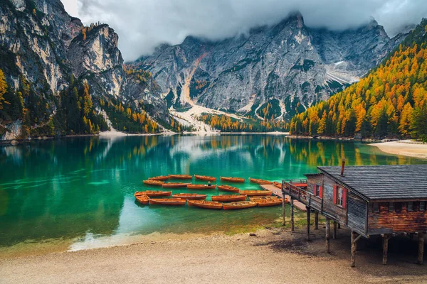 湖の上に木製の観光ボートと美しい秋の風景 湖のほとりにカラフルなカラフルなカラマツの木造ボートハウス線 ドロマイト イタリア ヨーロッパ — ストック写真