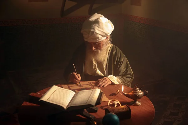 An old and historic Islamic scientist is working in his studio writing, reading and exploring.