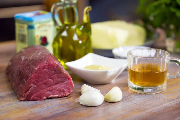 Preperation to cook a beef dish with all necessary ingredients are on a wooden table.