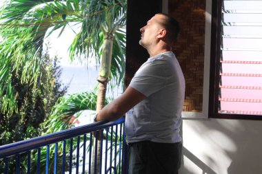 Bir adam bir balkon tropikal üzerinde duruyor ve denize görünüyor