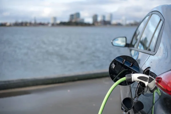 Ładowania samochodów elektrycznych, z miasta i wody w podłoże, zielony kabel do ładowania i czarny samochód. Kopenhaga — Zdjęcie stockowe