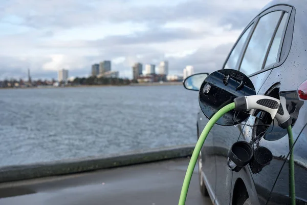 Charging an electric car, with the city and water in the background, green charging cable and black car. copenhagen