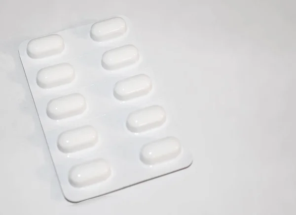 Packs of white pills packed in blisters with copy space isolated on a white background. Focus on foreground, soft bokeh. Pharmacy drugstore concept.