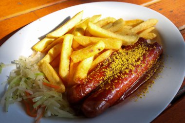 Geleneksel Alman körili sosisi, beyaz tabakta cips ile servis edilir. Arkaplan olarak turuncu tahta tablo.