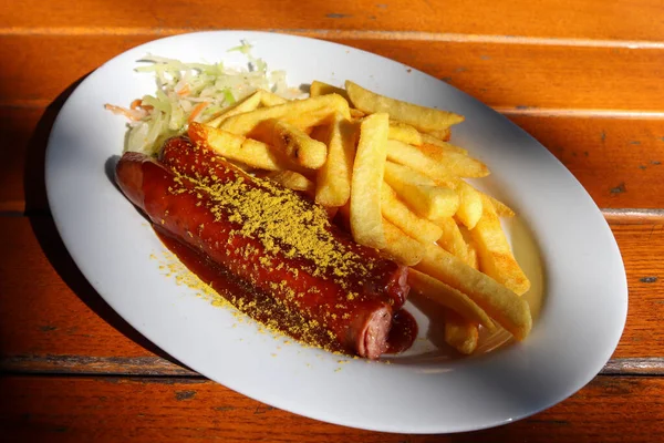 Tradycyjny Niemiecki Currywurst Podawany Chipsami Białym Talerzu Pomarańczowy Drewniany Stół — Zdjęcie stockowe