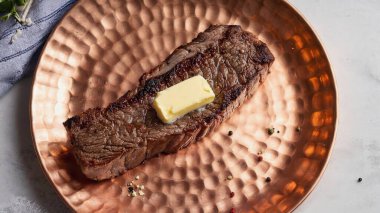 Bakır bir tabakta servis edilen tuzlu, biberli ve baharatlı erimiş tereyağlı ızgara biftek.