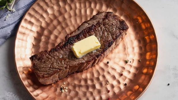 Bakır bir tabakta servis edilen tuzlu, biberli ve baharatlı erimiş tereyağlı ızgara biftek.