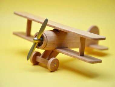 Sarı arka planda altın pervaneli küçük tahta çift kanatlı uçak çocukluğu, seyahati ve hayallerin peşinden koşmayı çağrıştırıyor.