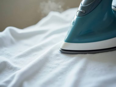 Beyaz bir gömleğin üzerinde süzülen buhar ütüsünün yakın çekimi, kırışıklıkları ve kırışıklıkları ortadan kaldırır.